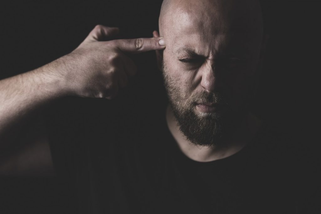 Man pointing his right index finger at his temple, like a pistol, eyes closed.